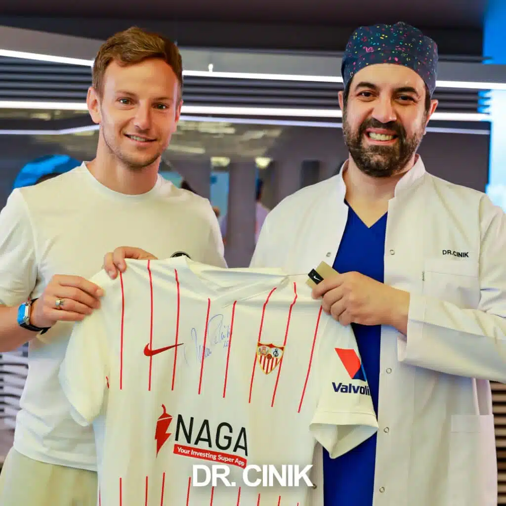 Dr. Cinik posing with Croatian footballer Ivan Rakitic, a World Cup finalist and Sevilla FC player, holding a Sevilla FC jersey at Dr. Cinik's hair transplant clinic in Istanbul, Turkey