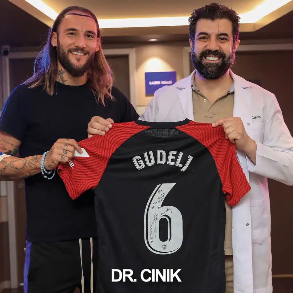 Dr. Cinik posing with Serbian international and Sevilla FC midfielder Nemanja Gudelj holding a Sevilla FC jersey with Gudelj's name and number 6 at Dr. Cinik's hair transplant clinic in Istanbul, Turkey