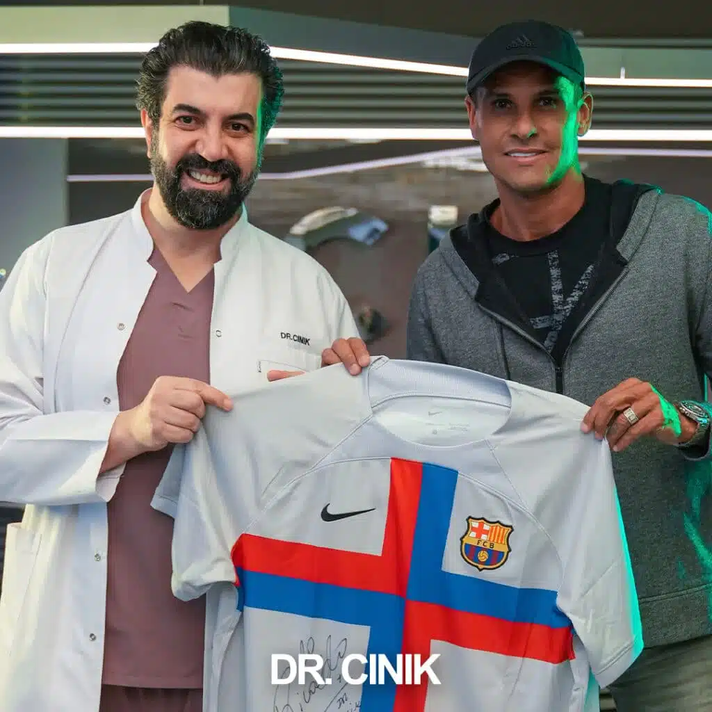Dr. Cinik posing with Brazilian football legend Rivaldo, Ballon d'Or winner and World Cup champion, holding a Barcelona jersey at Dr. Cinik's hair transplant clinic in Istanbul, Turkey